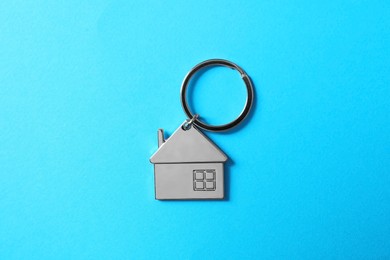 Metallic keychain in shape of house on light blue background, top view