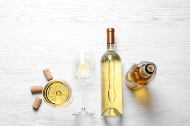 Photo of Glasses and bottles with white wine on wooden background, flat lay