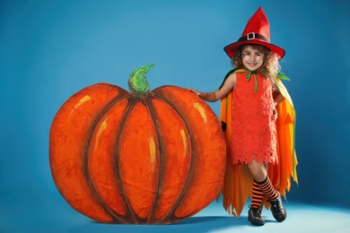 Photo of Cute little girl with decorative pumpkin wearing Halloween costume on light blue background