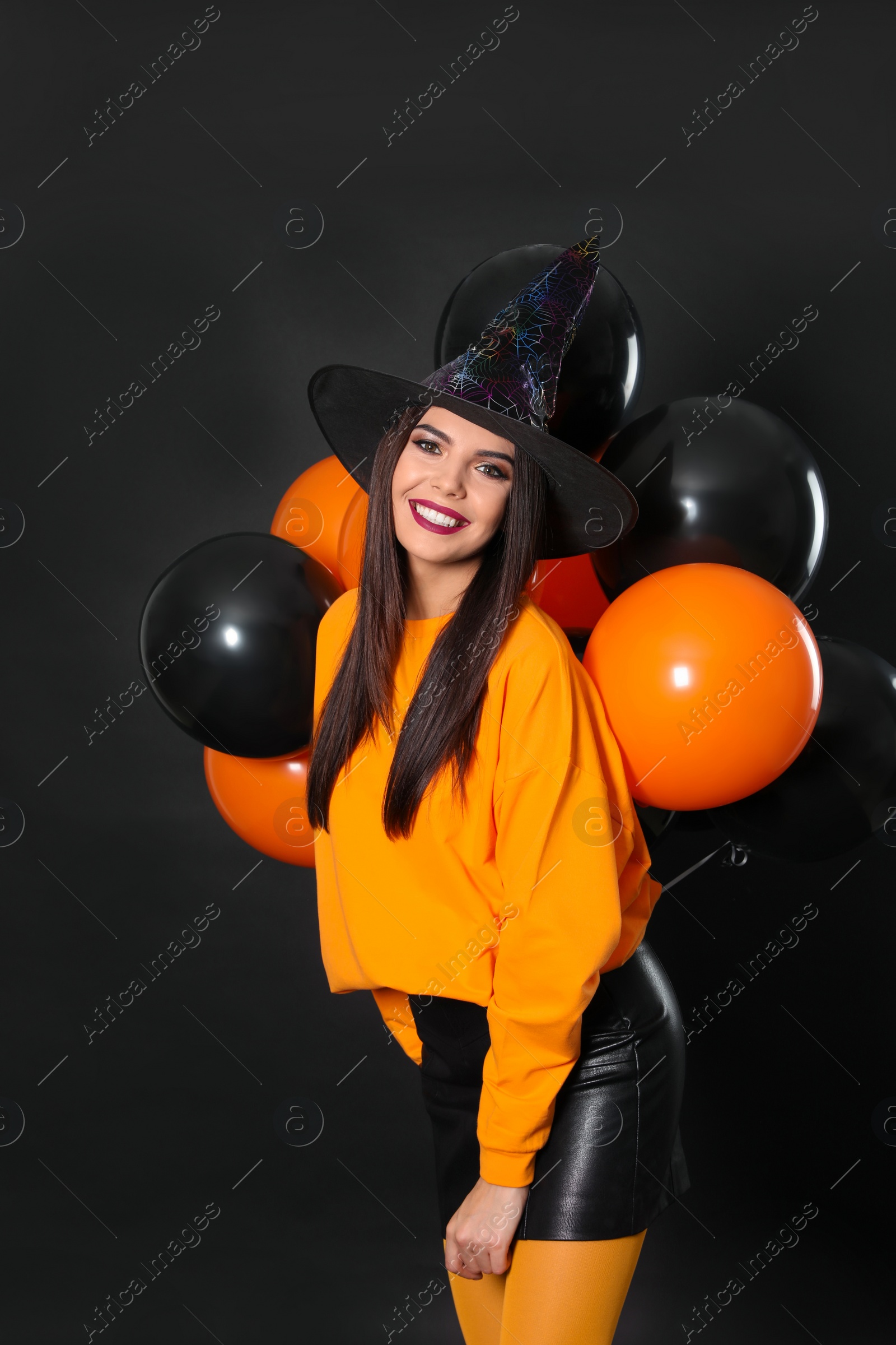 Photo of Beautiful woman wearing witch costume with balloons for Halloween party on black background