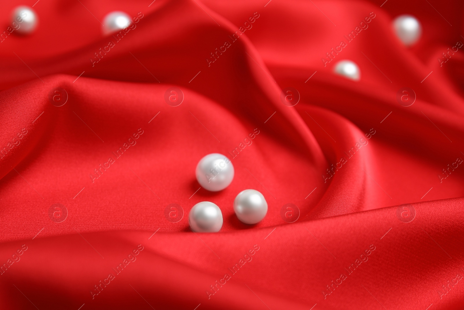 Photo of Many beautiful pearls on delicate red silk, closeup