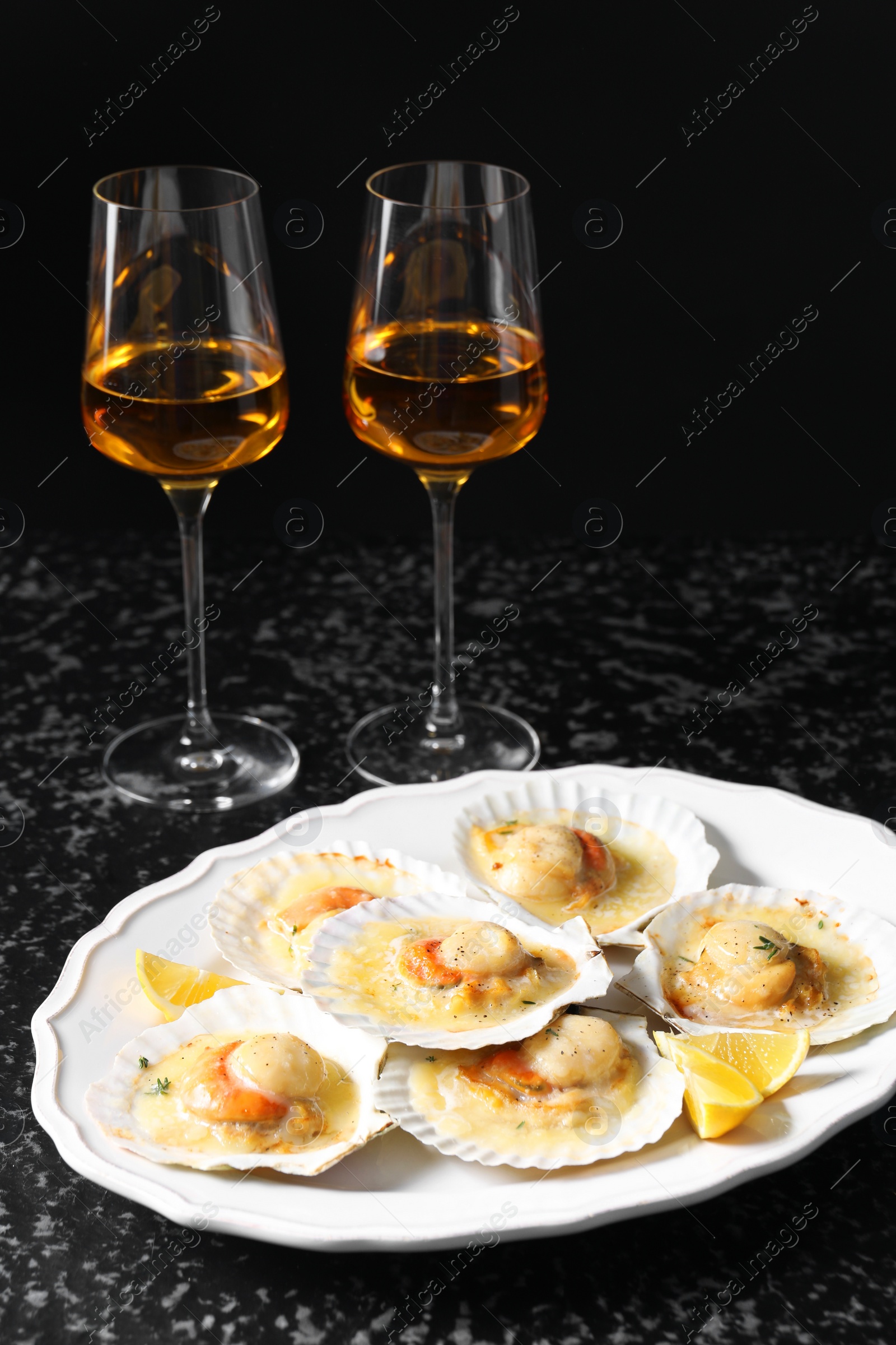 Photo of Fried scallops in shells and wine on black textured table