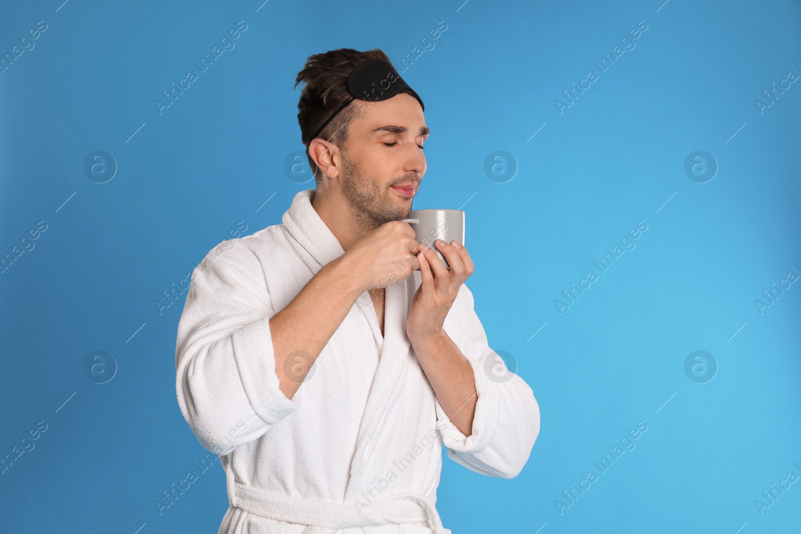 Photo of Young man in bathrobe with cup of coffee on light blue background