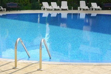 Outdoor swimming pool with ladder and handrails on sunny day