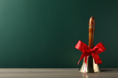 Golden bell with red bow on wooden table near green chalkboard, space for text. School days