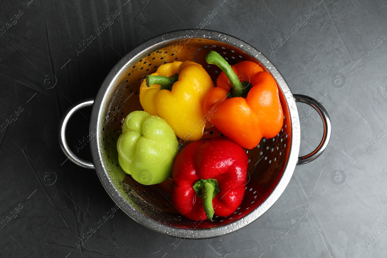 Photo of Colander with wet ripe bell peppers on grey table, top view