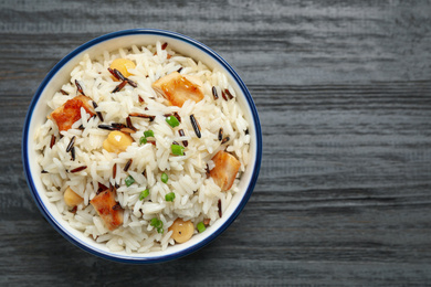 Photo of Delicious rice pilaf with chicken on black wooden table, top view. Space for text