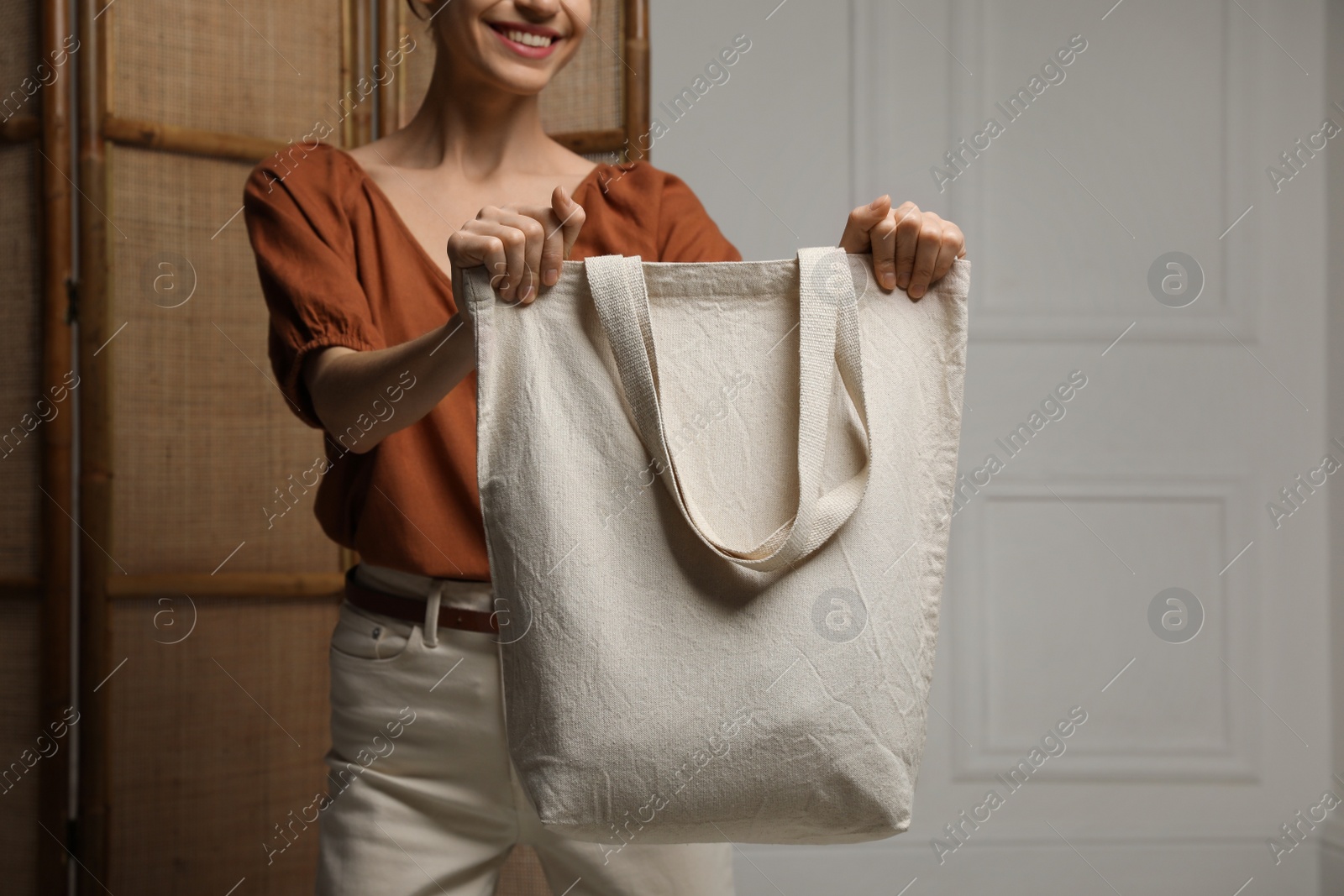 Photo of Happy young woman with blank eco friendly bag indoors, closeup