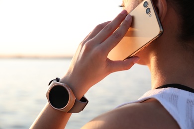 Photo of Woman with fitness tracker talking on phone near river, closeup