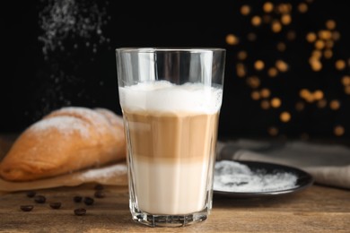 Delicious latte macchiato, croissant and scattered coffee beans on wooden table