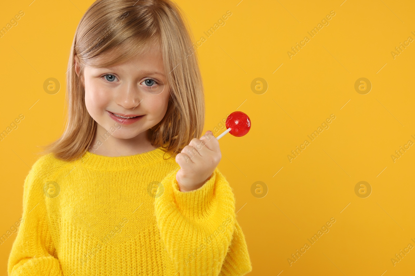 Photo of Happy girl with lollipop on orange background. Space for text