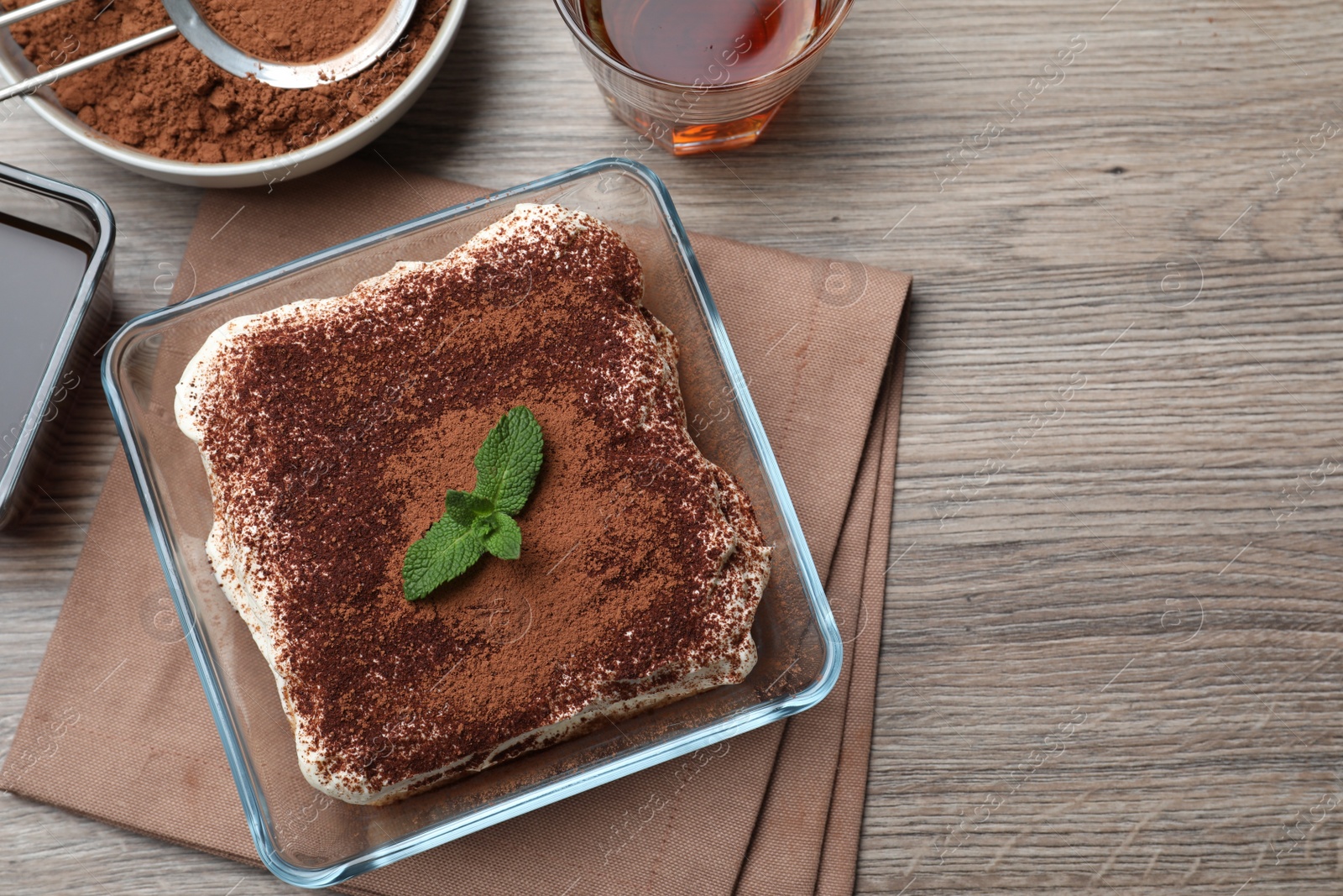 Photo of Glass bowl with delicious tiramisu cake on wooden table, flat lay. Space for text