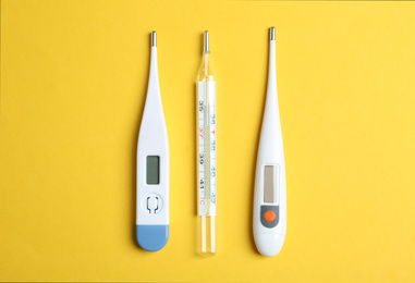 Different thermometers on yellow background, flat lay