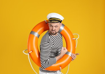 Photo of Serious sailor with orange ring buoy showing biceps on yellow background