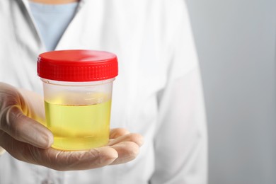 Photo of Doctor holding container with urine sample for analysis on grey background, closeup