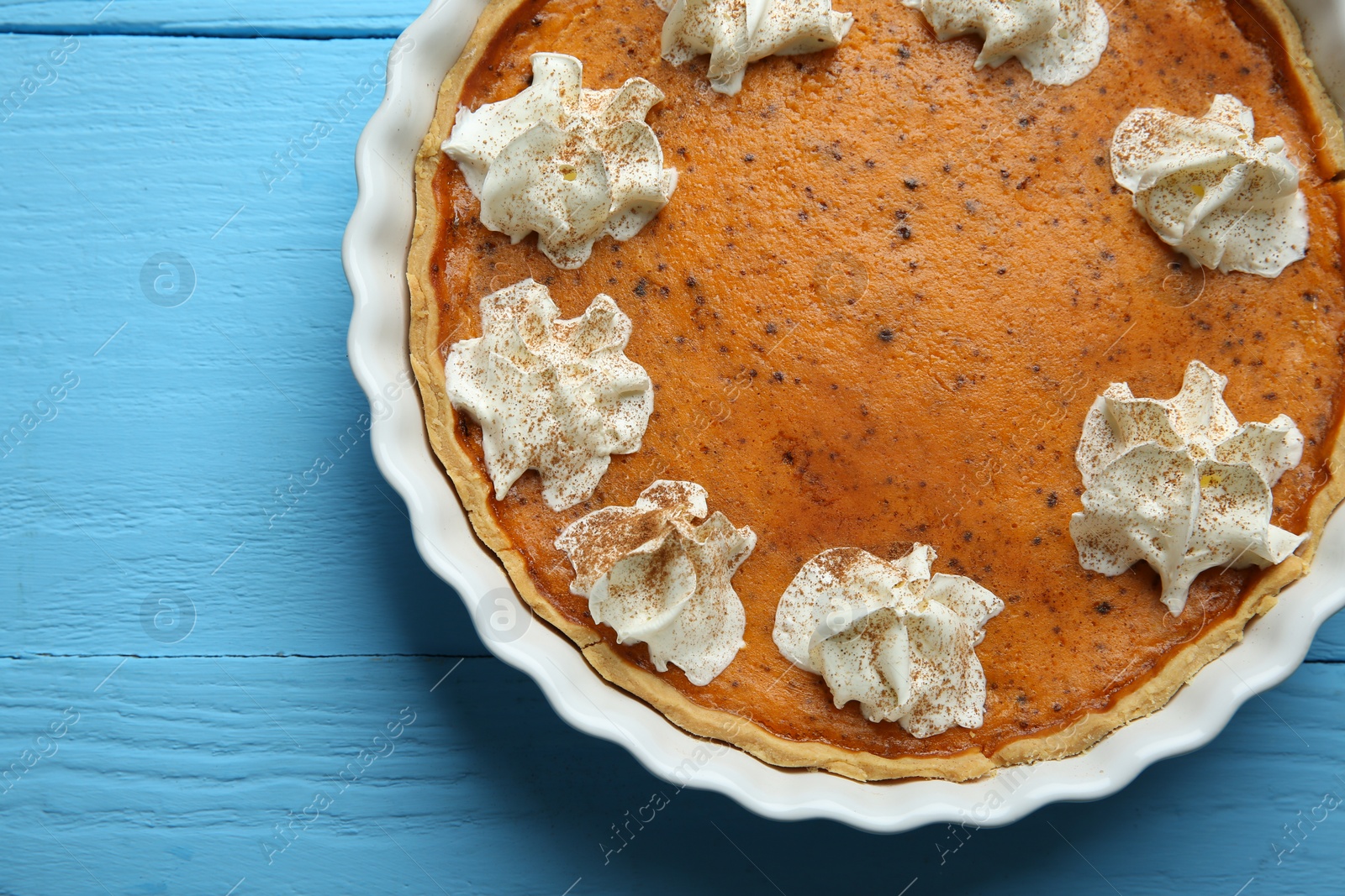 Photo of Delicious pumpkin pie with whipped cream on light blue wooden table, top view. Space for text