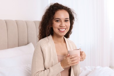 Photo of Happy African American woman with cup of drink in bed at home