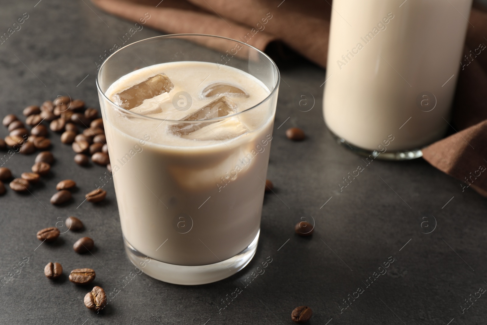 Photo of Coffee cream liqueur in glass and beans on grey table, closeup