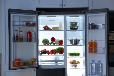 Photo of Open refrigerator full of different products in kitchen