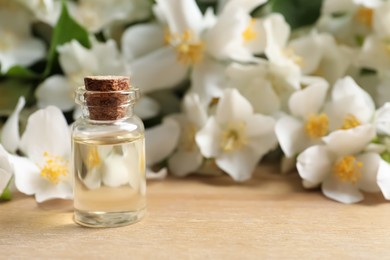 Jasmine essential oil and fresh flowers on wooden table, space for text