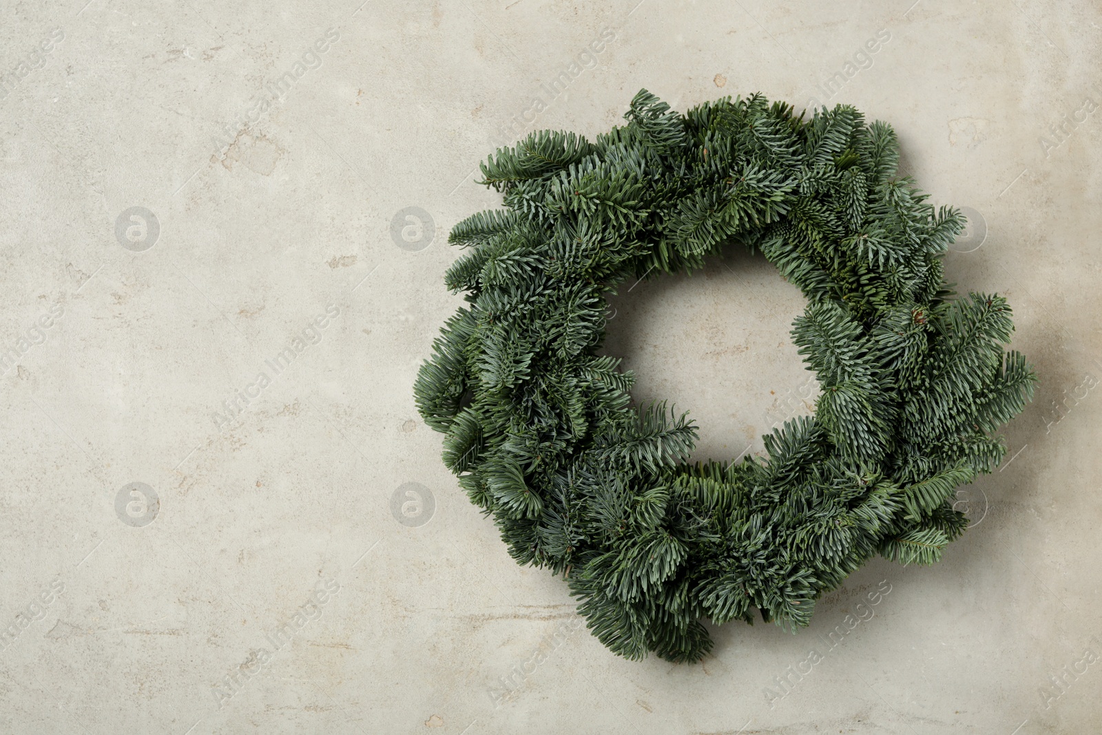 Photo of Christmas wreath made of fir tree branches on light grey background, space for text