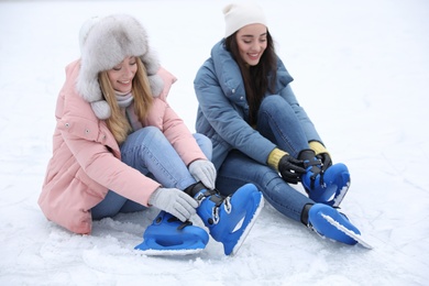 Photo of Happy women with figure skates sitting on ice rink outdoors