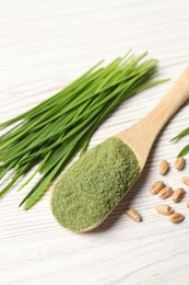 Wheat grass powder in spoon, seeds and fresh sprouts on white wooden table, closeup