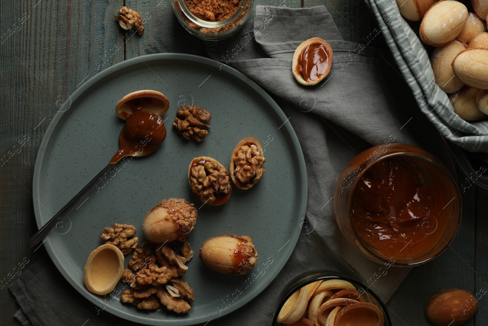 Photo of Freshly baked homemade walnut shaped cookies with nuts and boiled condensed milk on wooden table, flat lay