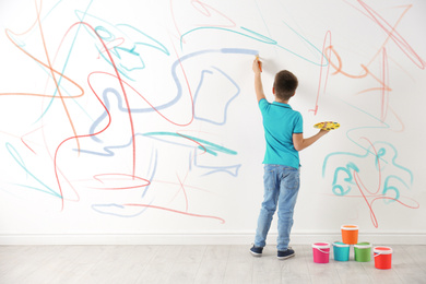 Little child drawing scribbles on white wall indoors
