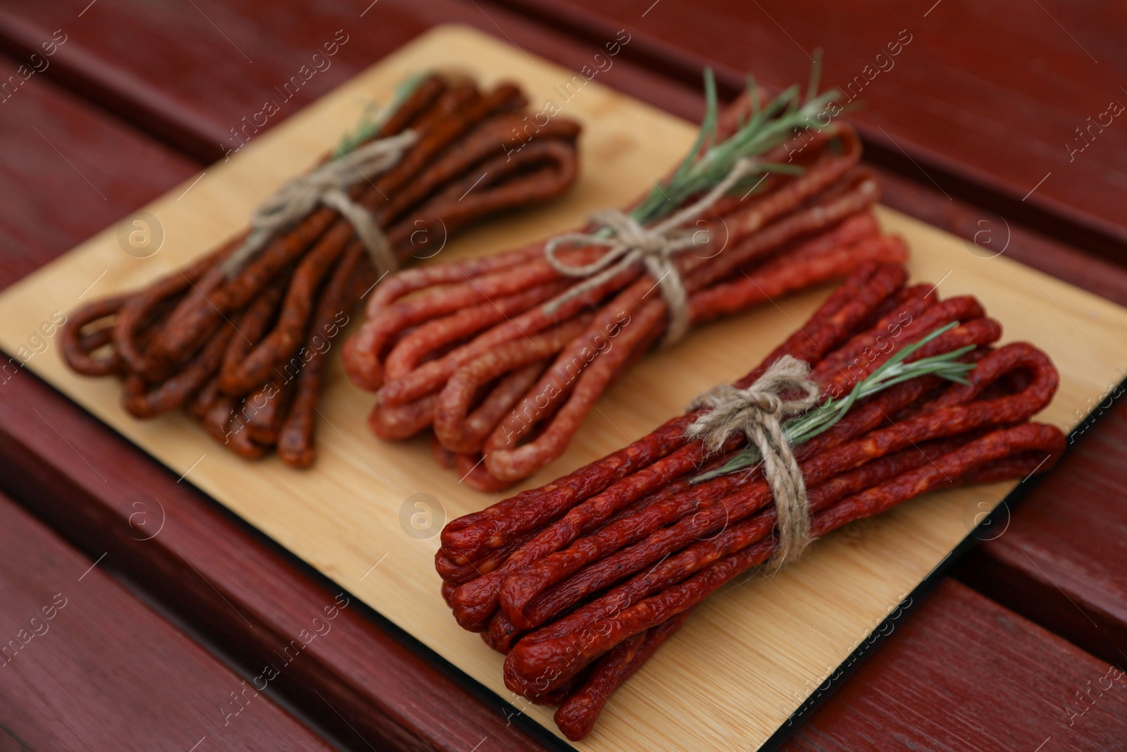 Photo of Bundles of delicious kabanosy with rosemary on wooden table, space for text