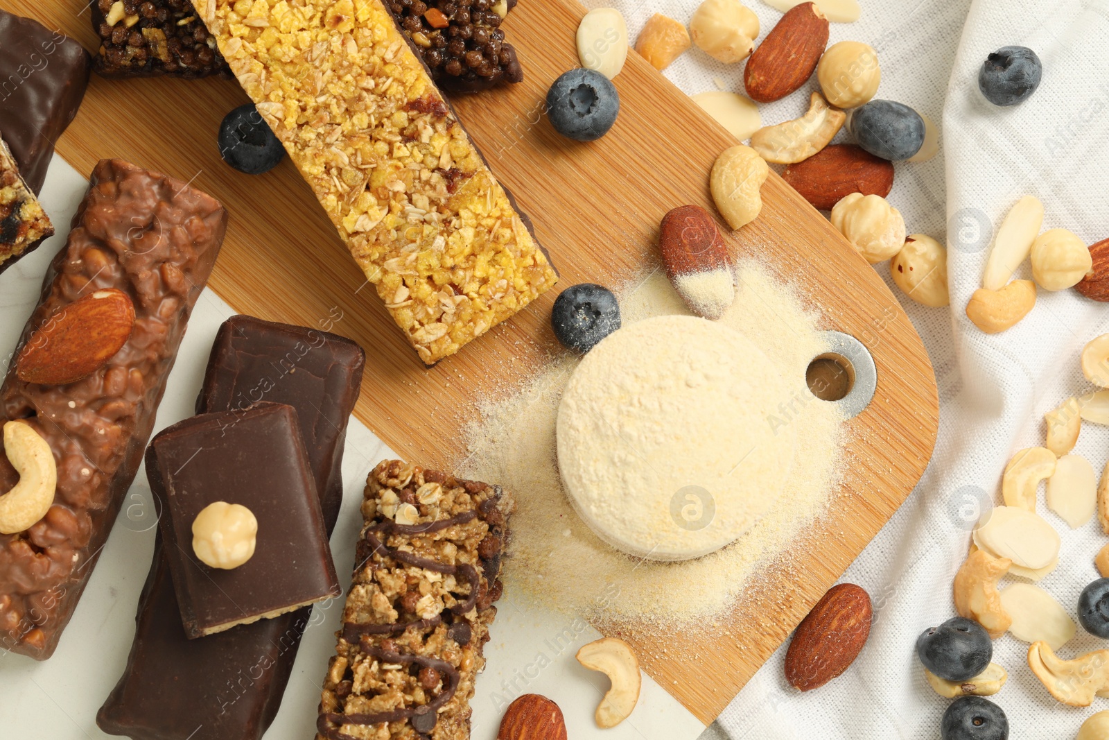 Photo of Different energy bars, nuts, blueberries and protein powder on table, flat lay