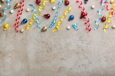 Photo of Shiny serpentine streamers and Christmas balls on grey background, flat lay. Space for text