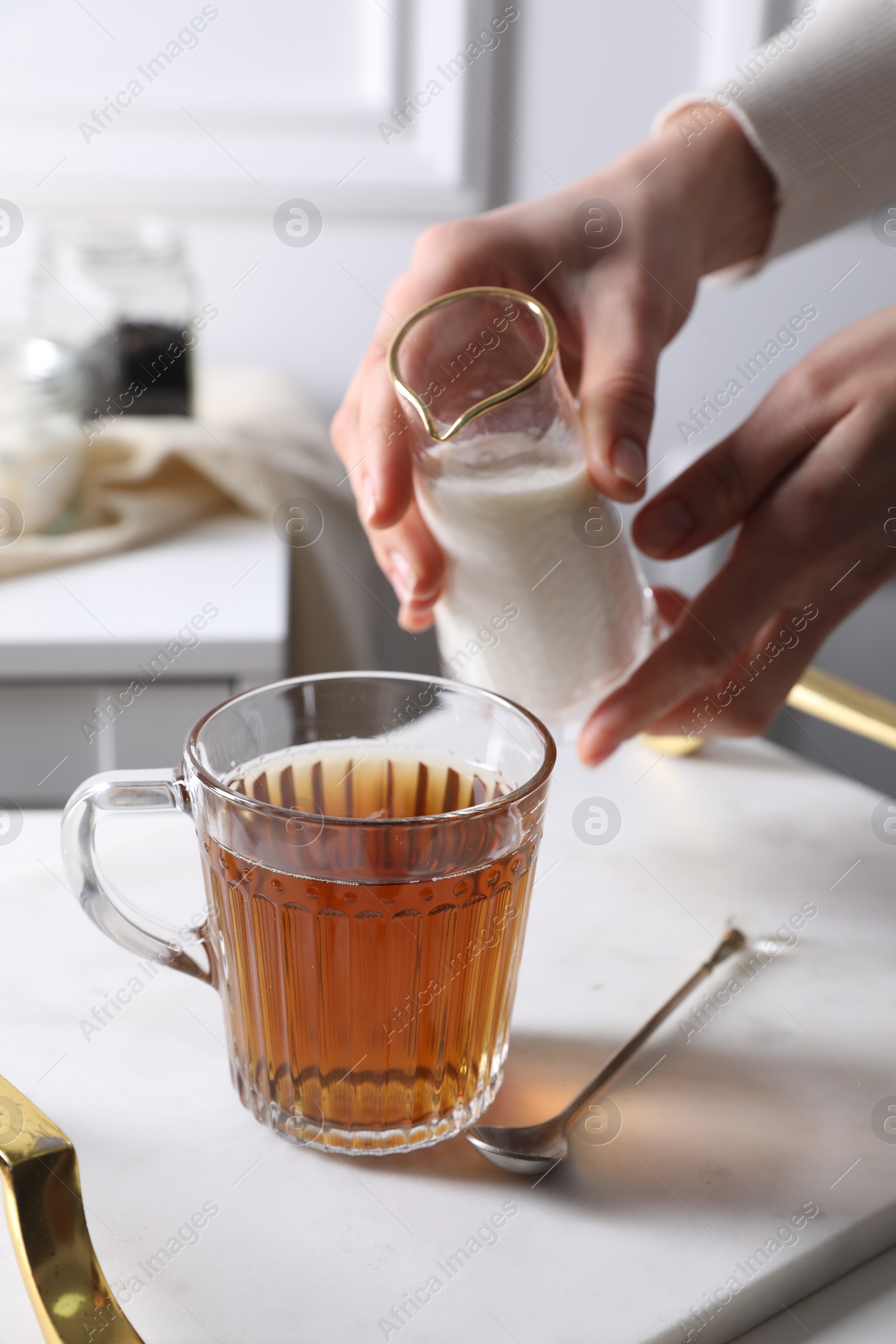 Photo of Woman pouring milk into cup of tea at white table, closeup