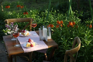 Photo of Vase with spring flowers, wine and cake on table served for romantic date in garden