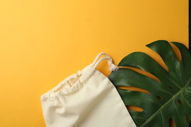 Cotton eco bag and leaf on yellow background, flat lay. Space for text