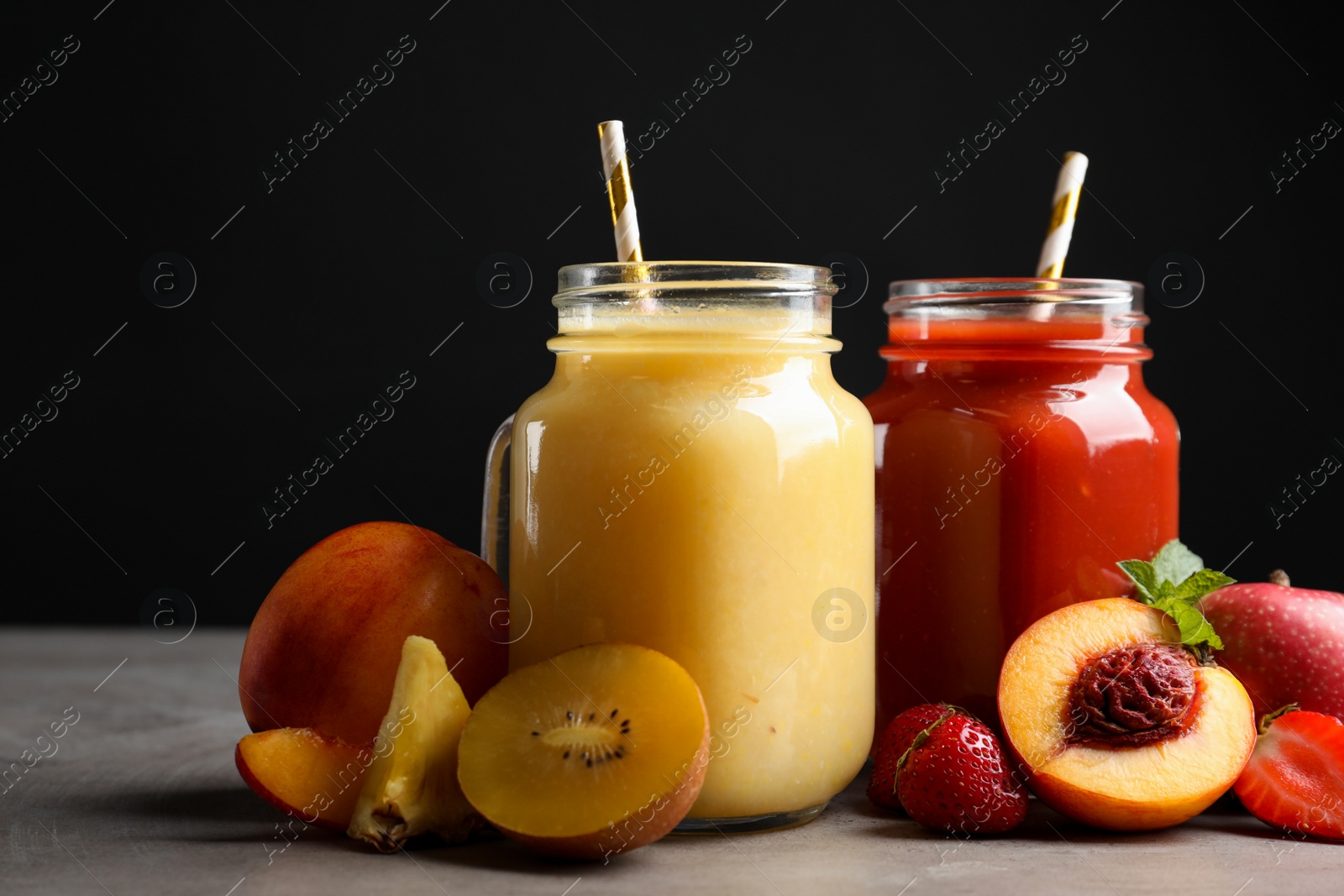 Photo of Delicious juices and fresh ingredients on grey table against black background