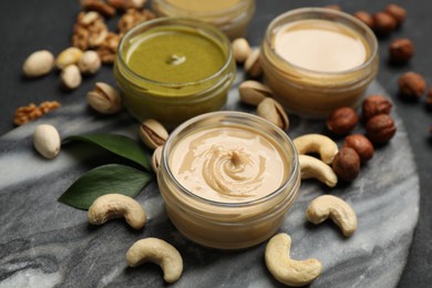 Jars with butters made of different nuts and ingredients on black table, closeup