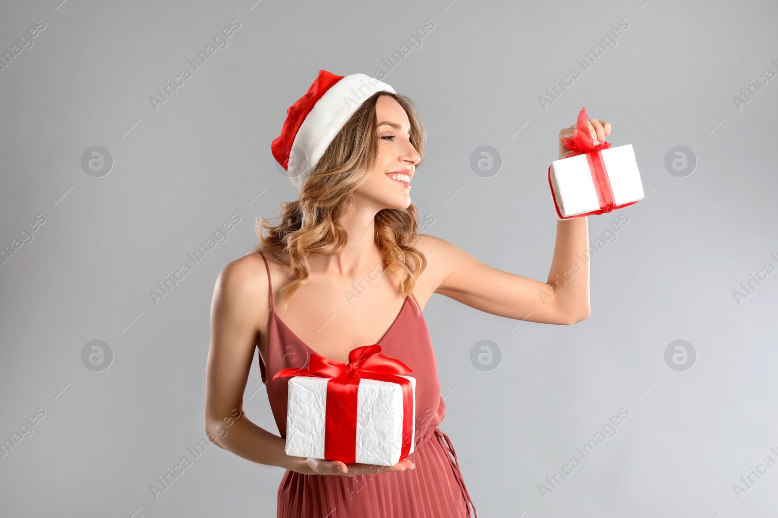 Photo of Beautiful young woman in Santa hat with Christmas presents on light grey background