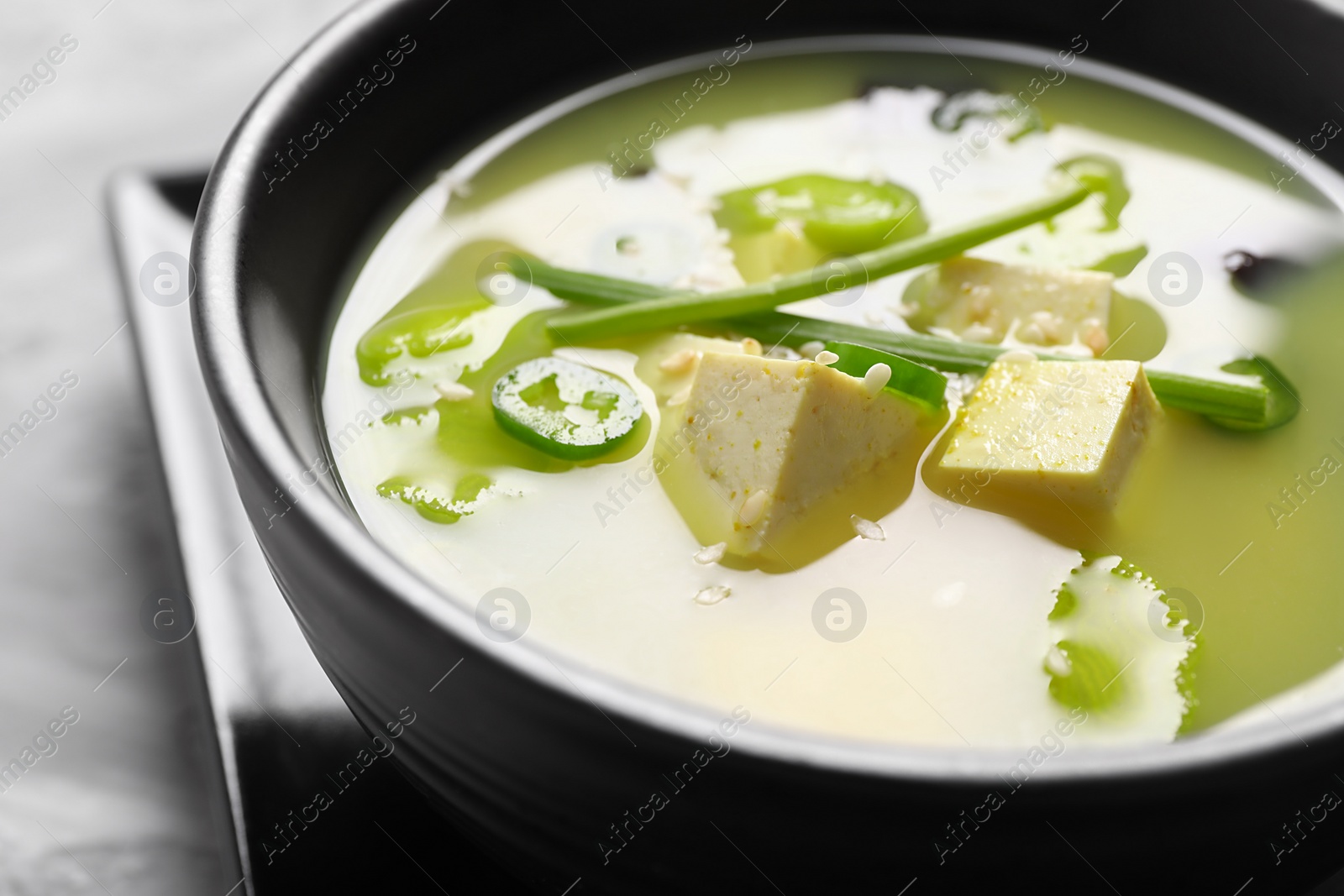 Photo of Bowl of delicious miso soup with tofu on table, closeup