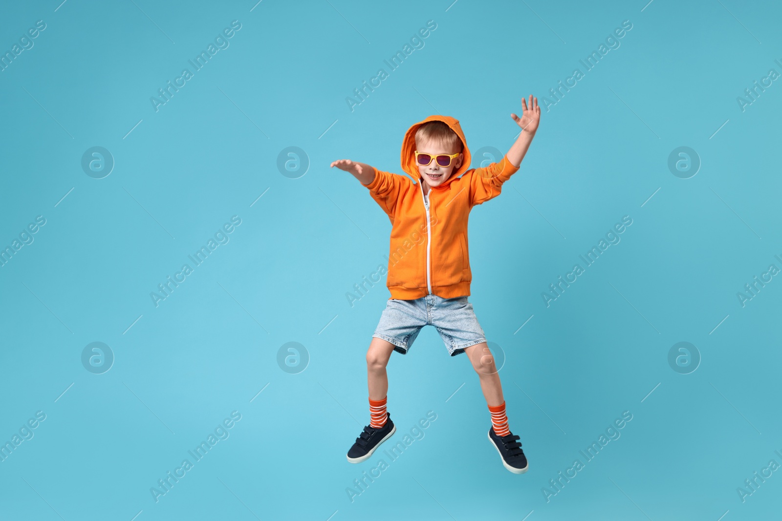 Photo of Happy little boy dancing on light blue background. Space for text