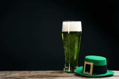 Photo of Green beer and hat on wooden table against black background, space for text. St. Patrick's Day celebration