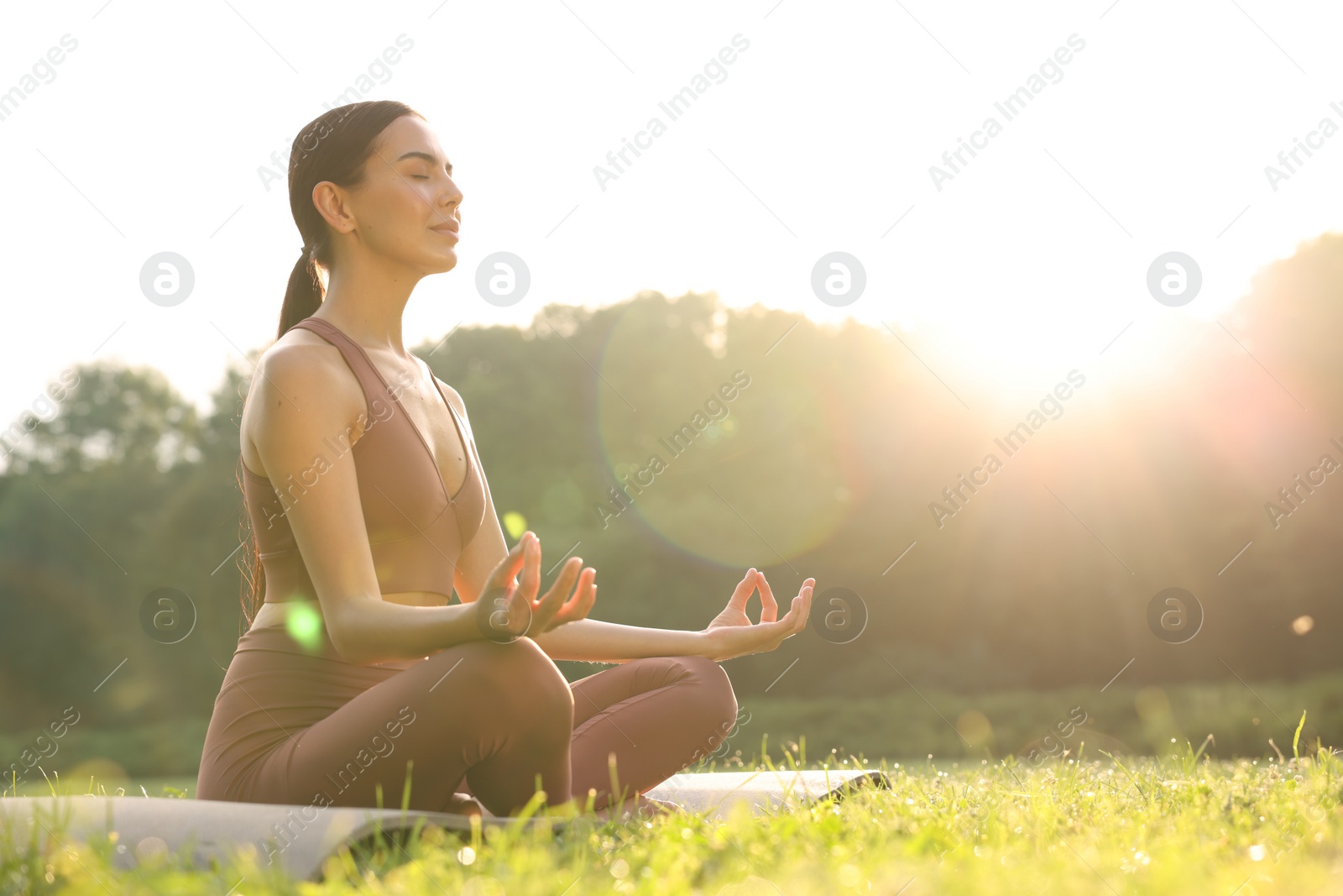 Photo of Beautiful young woman practicing Padmasana on yoga mat outdoors, low angle view and space for text. Lotus pose