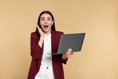 Shocked woman with laptop on beige background