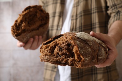 Photo of Man holding loaf of fresh broken bread near grey wall, closeup