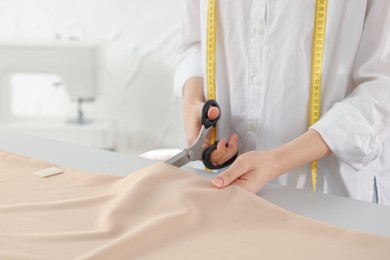 Photo of Dressmaker cutting fabric with scissors at table in atelier, closeup
