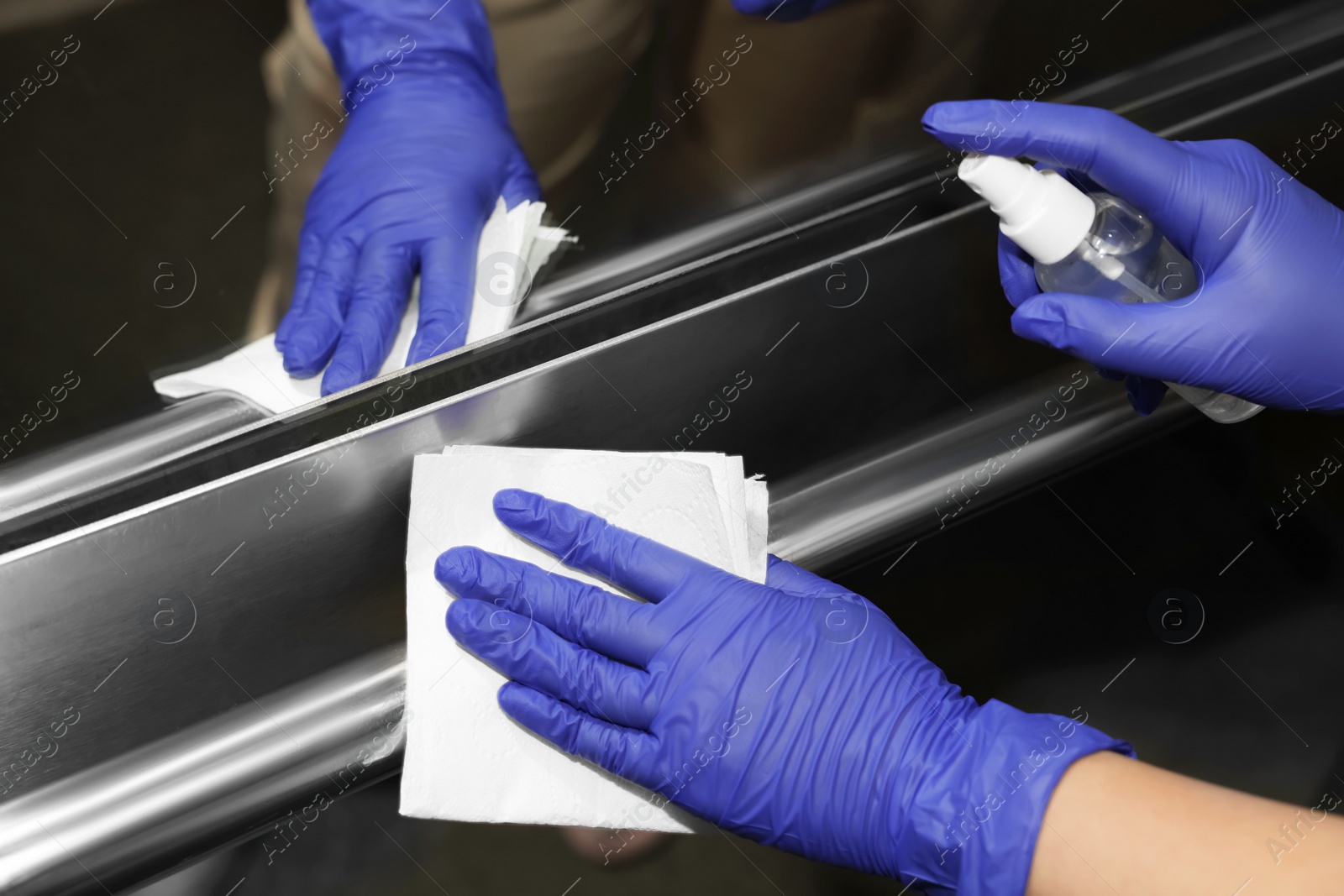 Photo of Woman wiping elevator`s handrails with detergent and paper napkin, closeup