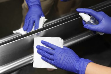 Photo of Woman wiping elevator`s handrails with detergent and paper napkin, closeup