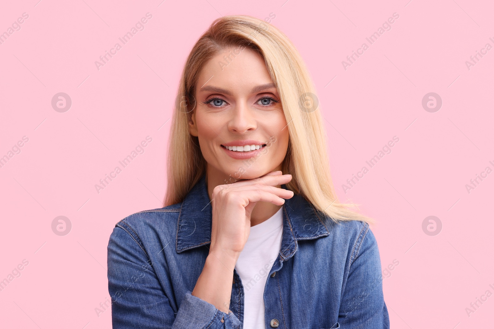 Photo of Portrait of smiling middle aged woman with blonde hair on pink background