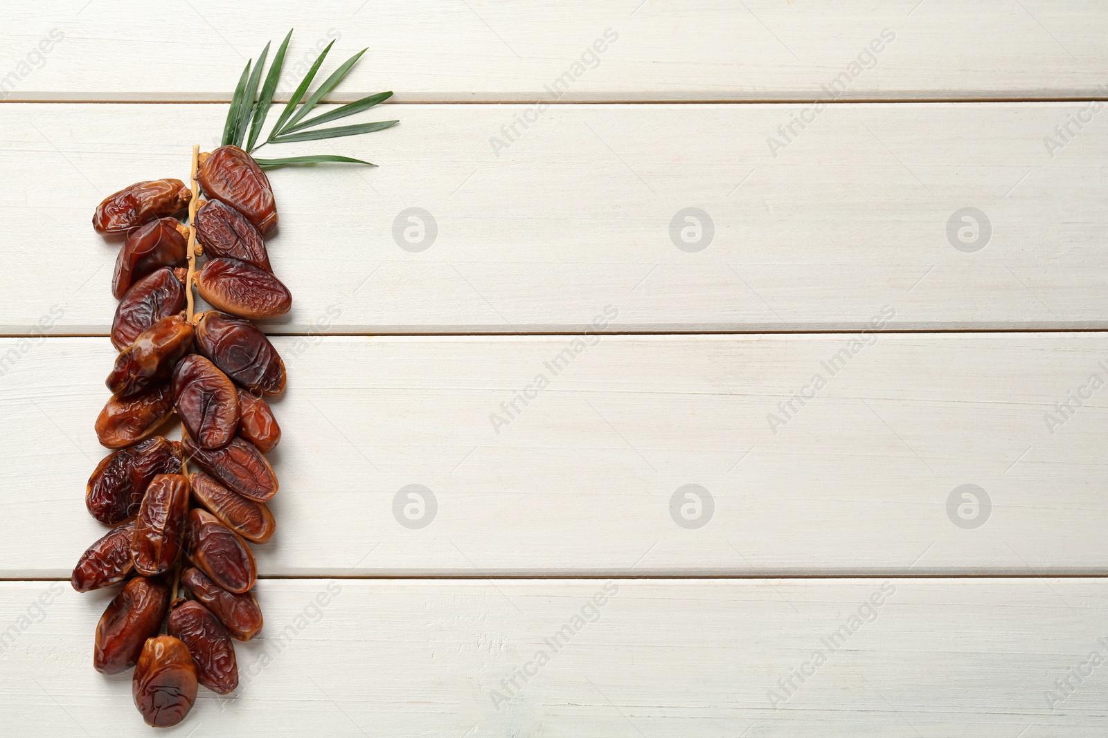 Photo of Branch of sweet dried dates and green leaves on white wooden table, top view. Space for text