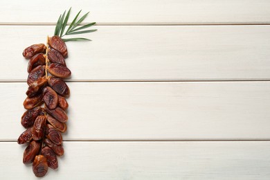 Branch of sweet dried dates and green leaves on white wooden table, top view. Space for text